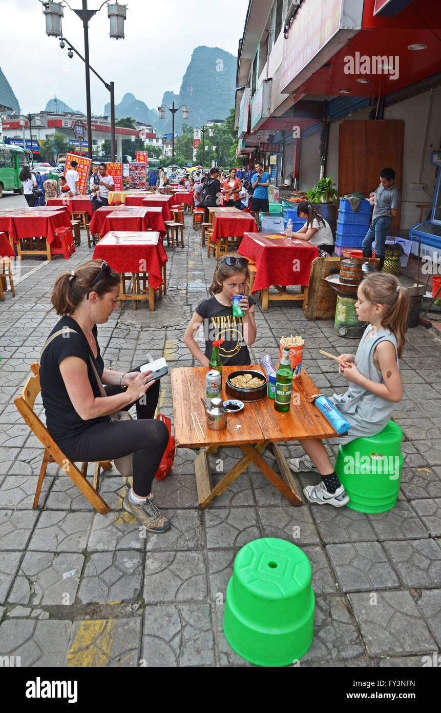 A family of tourists sits down for a meal of dumplings outside a restaurant in Yangshuo, China Stock Photo