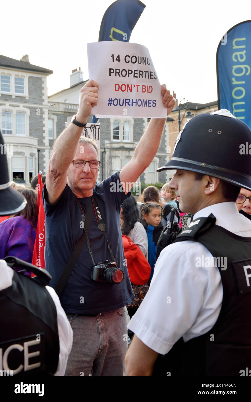 Bristol, UK. 20th April, 2016. Protest demonstration of Bristol City Council selling houses and flats by auction instead of refurbishing for residents. Protester holding plackard above heads of police to show to those entering the auction. Protest at All Saints Church on Pempbrooke Road, Bristol auction run by Hollis Morgan Property Ltd. attrated an estimated 100 protesters. Credit:  Charles Stirling/Alamy Live News Stock Photo