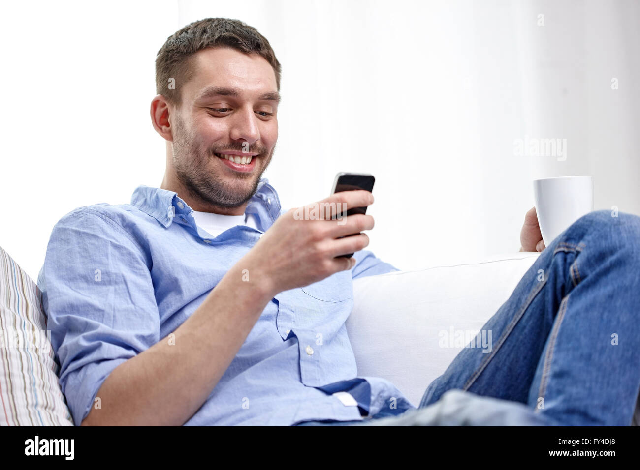 smiling man with smartphone at home Stock Photo