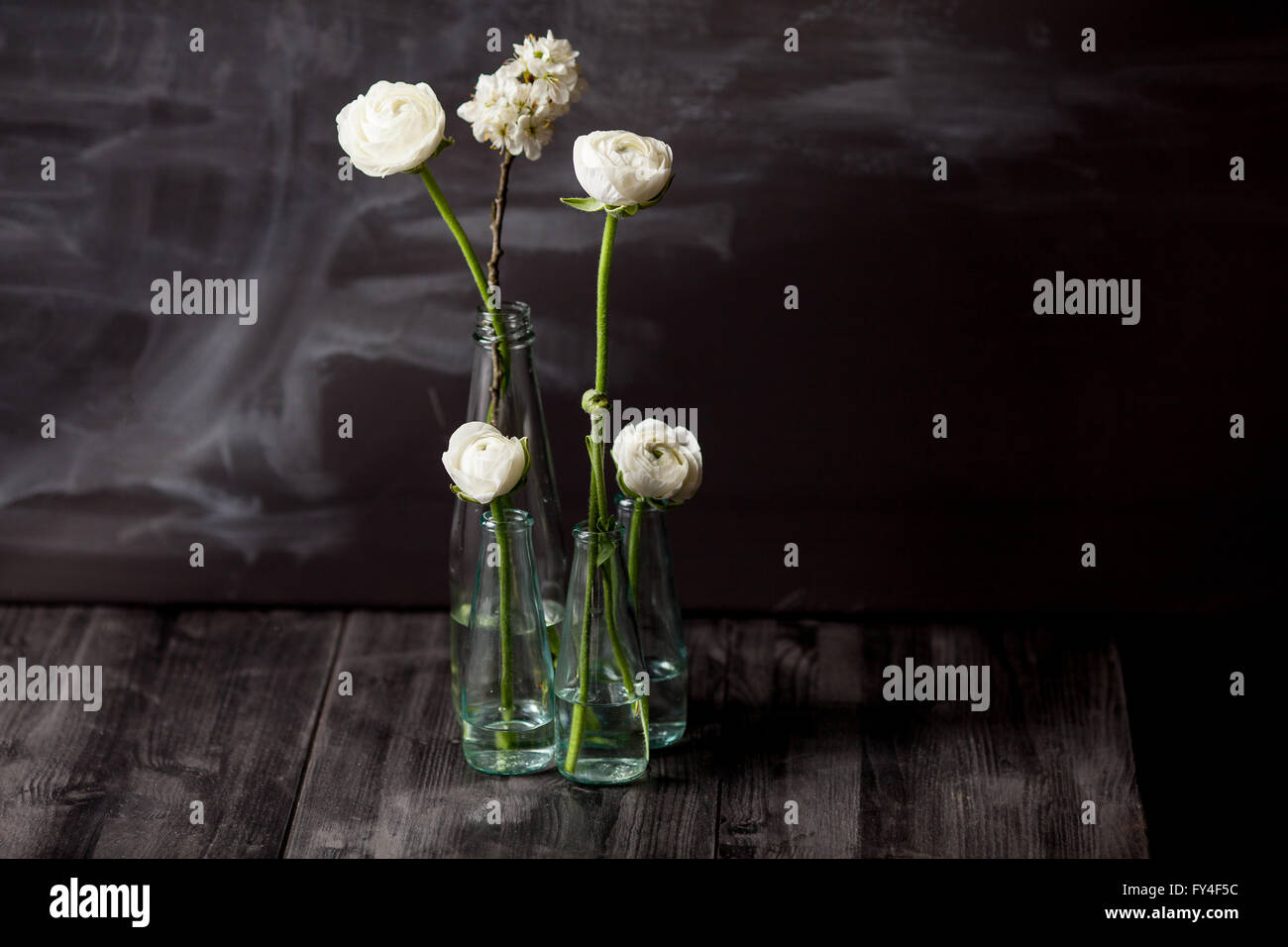 Four white buttercups and blossom apple in small, glass bottles