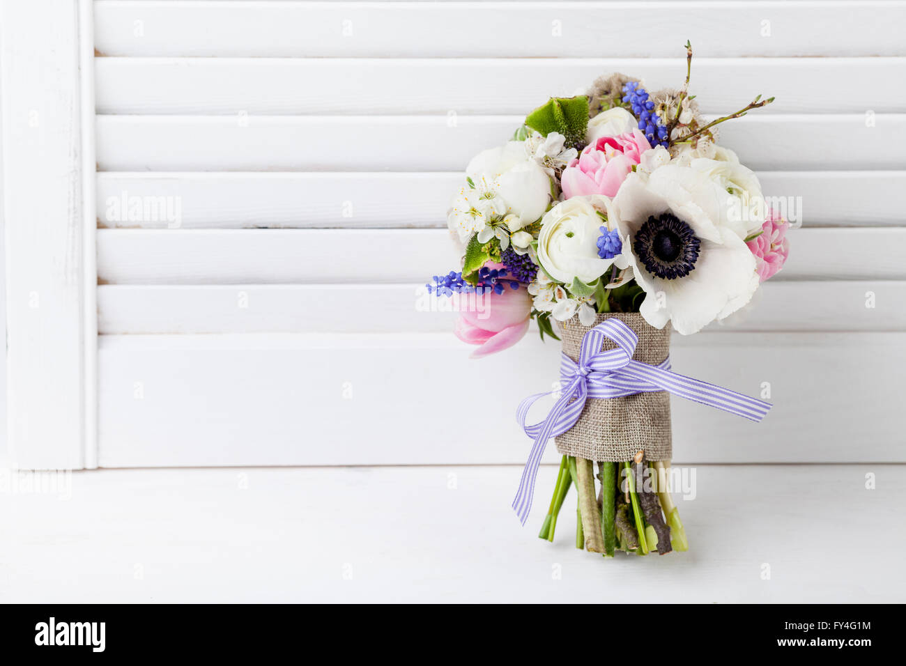Bouquet from pink tulips, violet grape hyacinths, white anemones, violet veronica and white buttercup with violet ribbon with wh Stock Photo