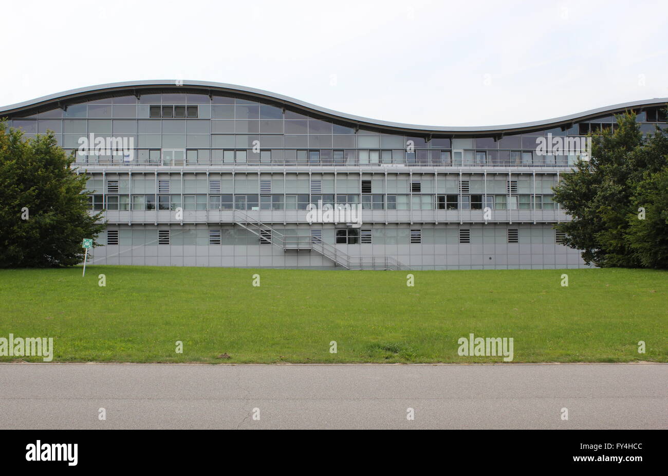 Modern science/industry building with wave shape. An assembly point sign can be seen on the left. Stock Photo