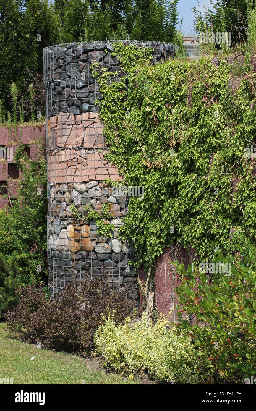 Wall with differently shaped stones in metal mesh. It is partly overgrown. Stock Photo