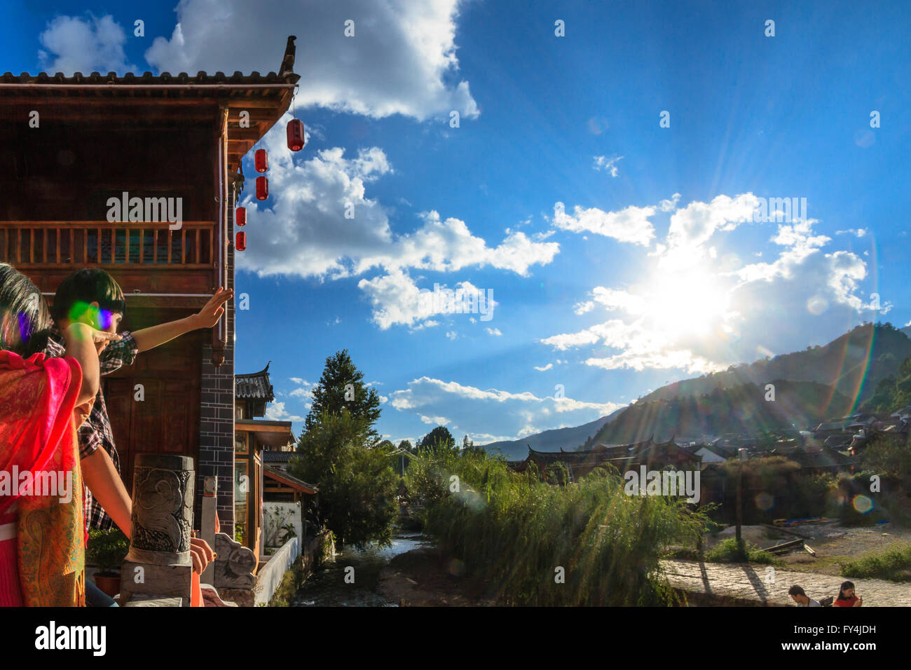 Chinese tourist couple watches the traditional village in front of mountain scenery and the setting sun. Stock Photo