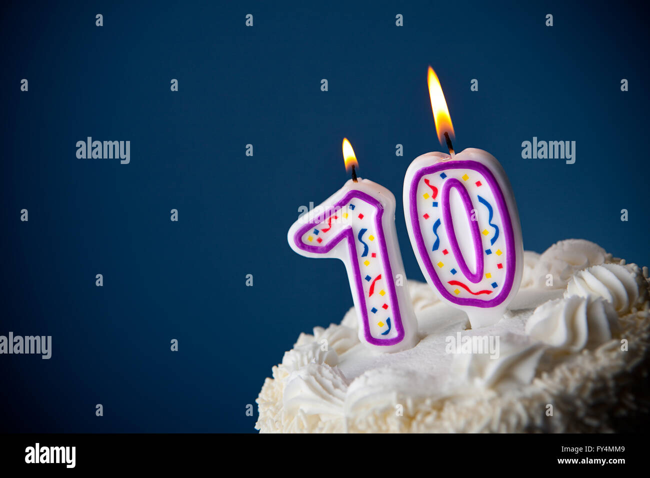 White iced cake on blue background with candles to celebrate various birthdays. Stock Photo