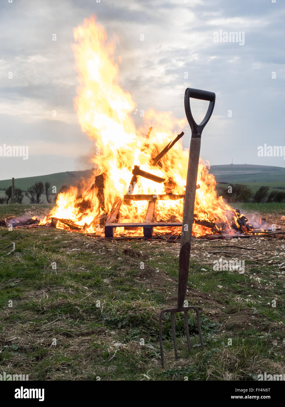 a garden fork dug in the ground in front of a lit fire beacon for queen's 90th birthday, in Whitwell, Isle of Wight, UK Stock Photo