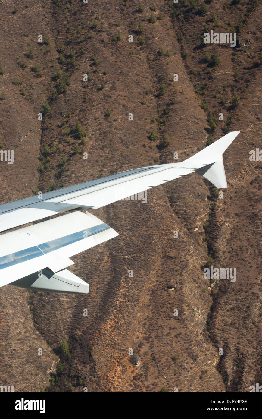 Wing of aeroplane flying through a steep narrow valley on approach to Paro, Bhutan Stock Photo