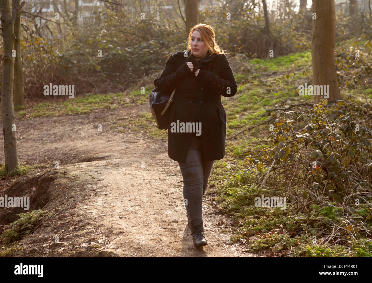 A woman is walking home through the park alone and she feels the fear that there could be someone behind her. Stock Photo