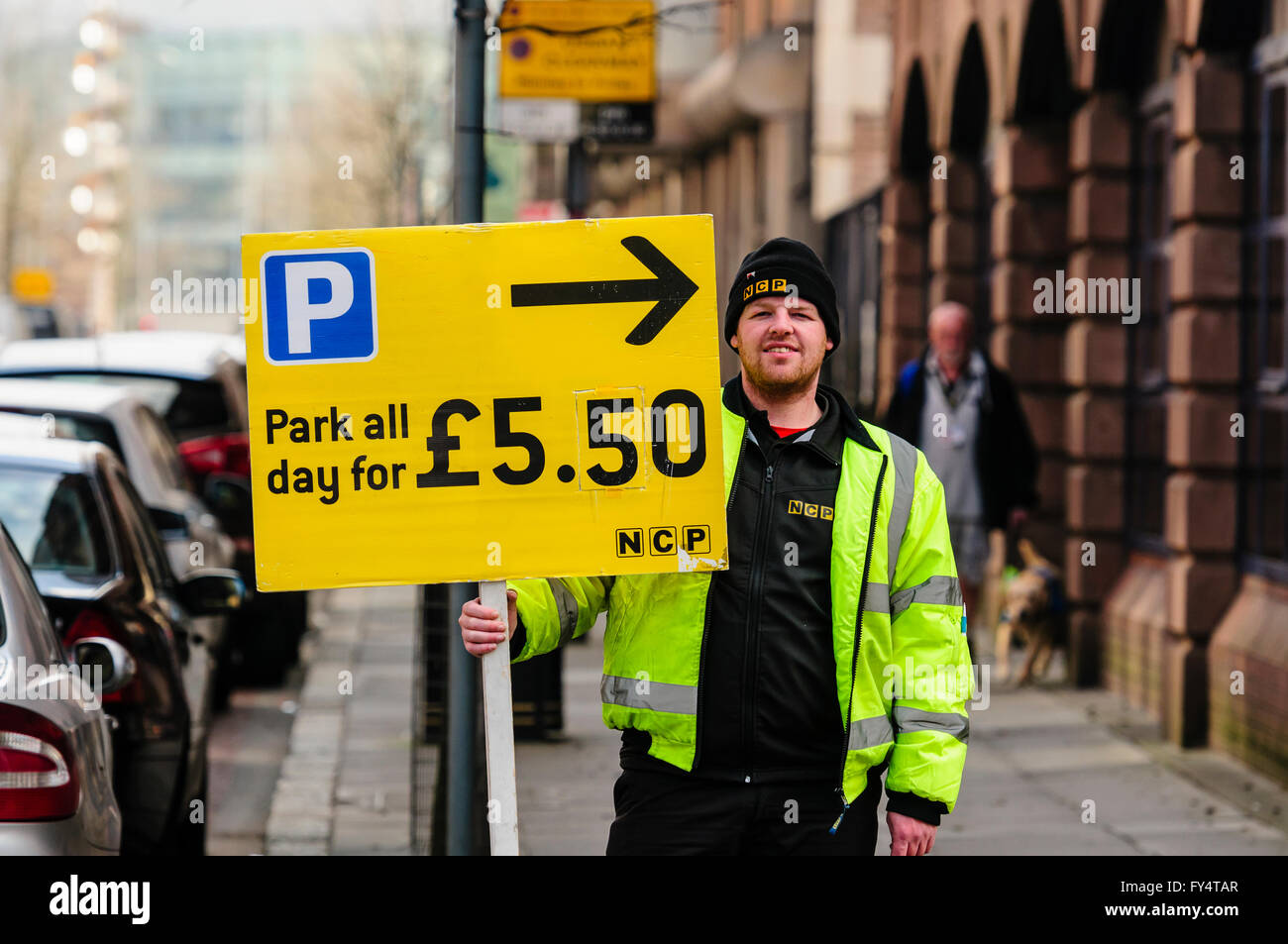 An NCP employee holds a sign directing motorists to all-day parking for £5.50 Stock Photo