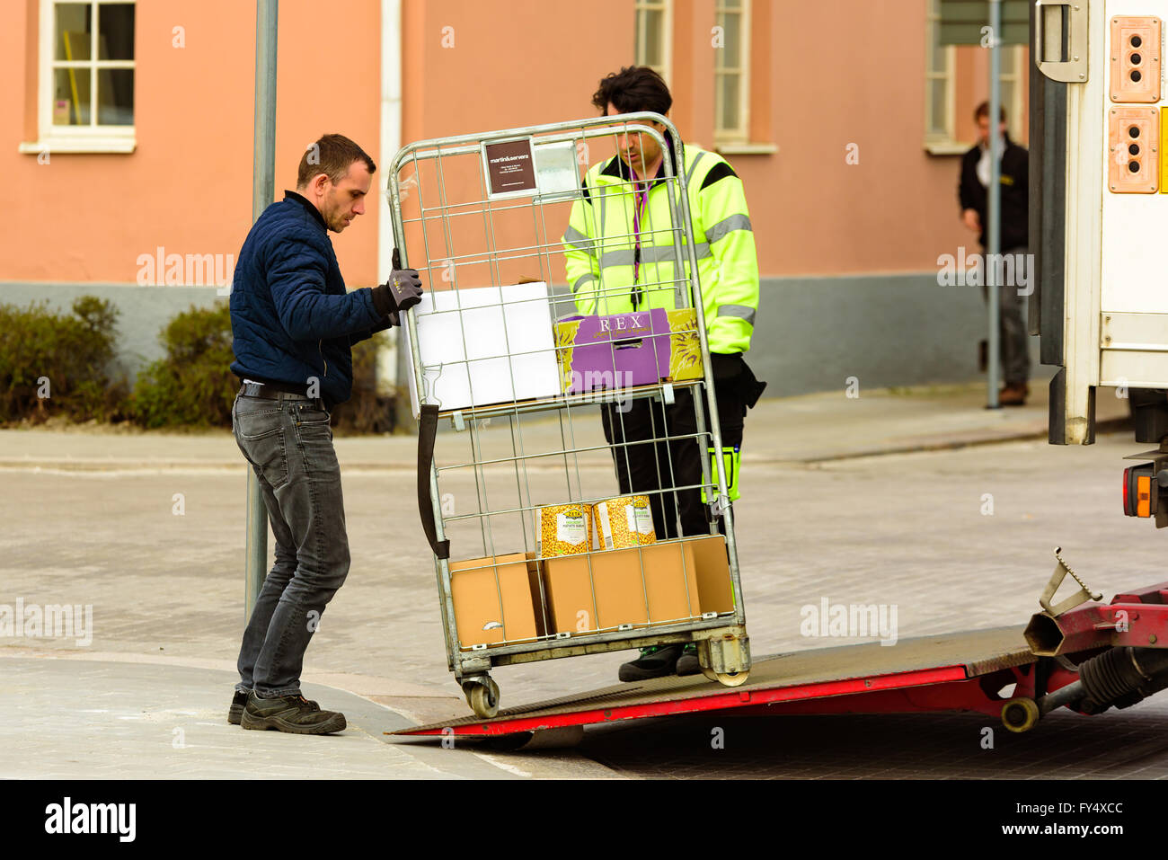 Trelleborg, Sweden - April 12, 2016: Two men are delivering a wire mesh rolling cart with merchandize from the back of a truck. Stock Photo