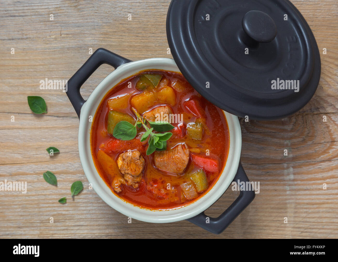 Goulash in a black cocotte with marjoram on rustic wood. Stock Photo