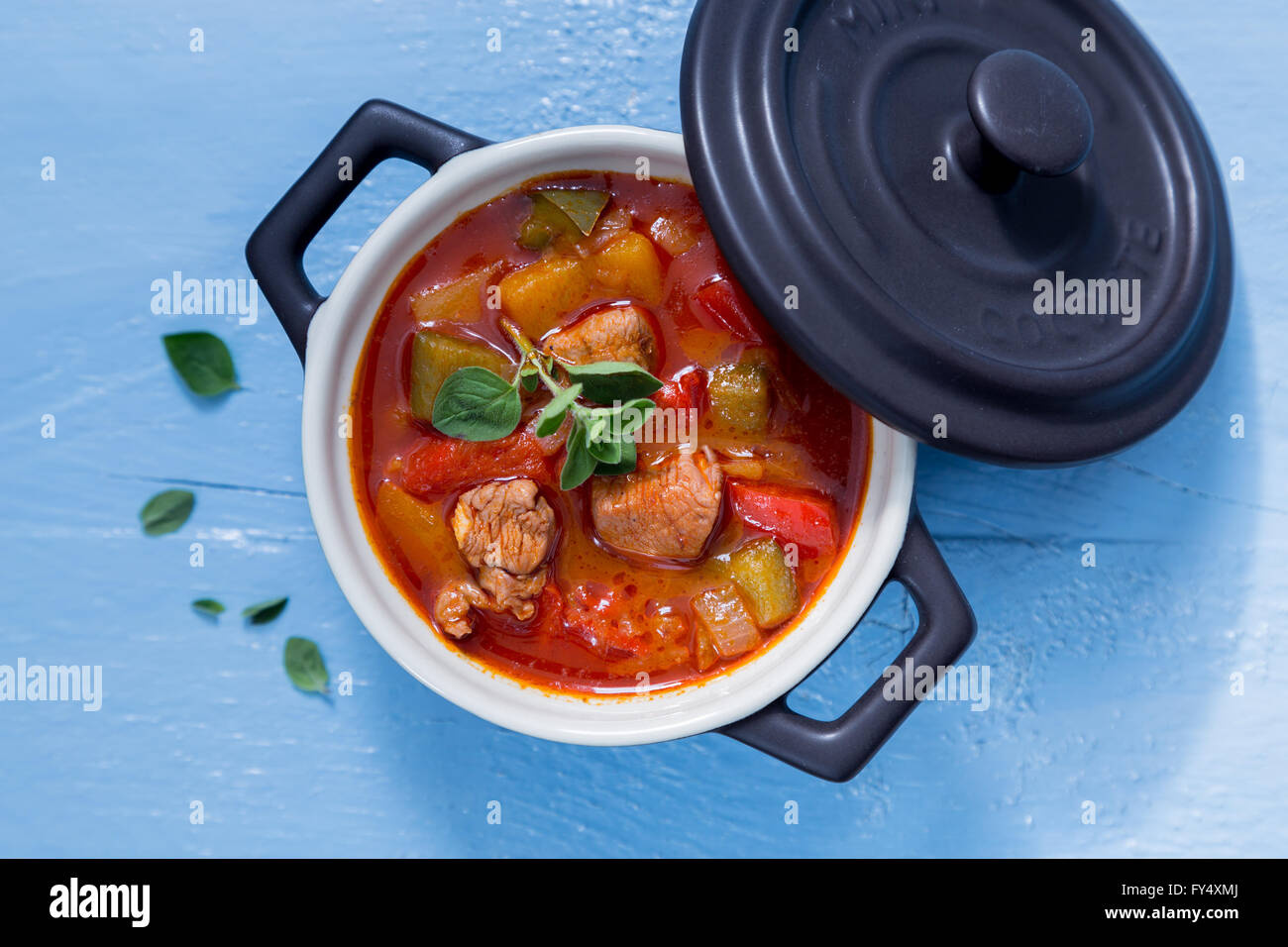 Goulash in a black cocotte with marjoram on blue wood. Stock Photo