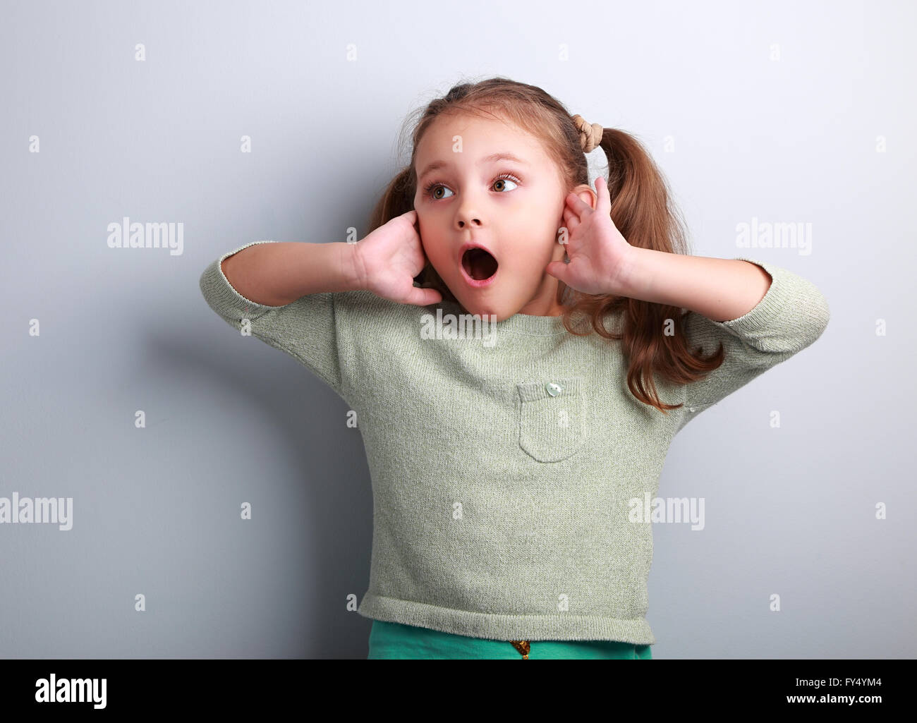 Surprising kid girl with opened mouth and hand near face looking on blue copy space background Stock Photo
