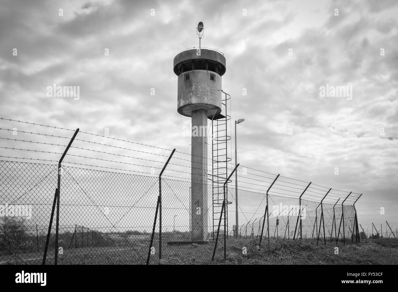 Abandoned watchtower isolated by a net topped with barbed wire. Stock Photo