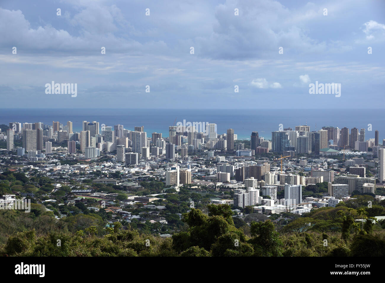 Honolulu cityscape, roads, buildings, skyscrapers, cranes, parks, and Pacific Ocean with clouds in the sky seen from up in the m Stock Photo