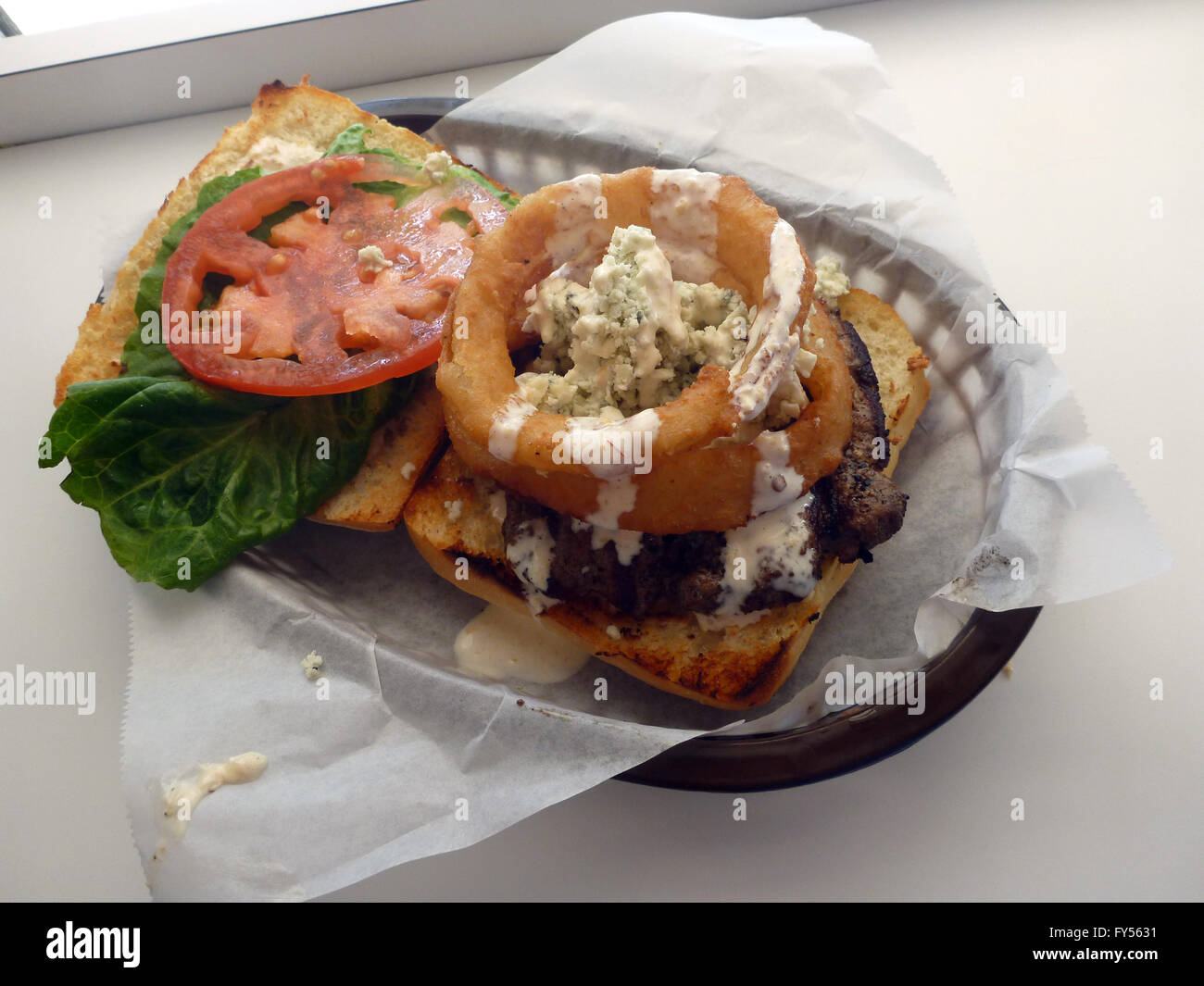 Blue Holes Burger Onion Rings Blue Cheese crumbles Ciabatta Aioli Lettuce and tomato in a plastic basket on a white table Stock Photo Alamy