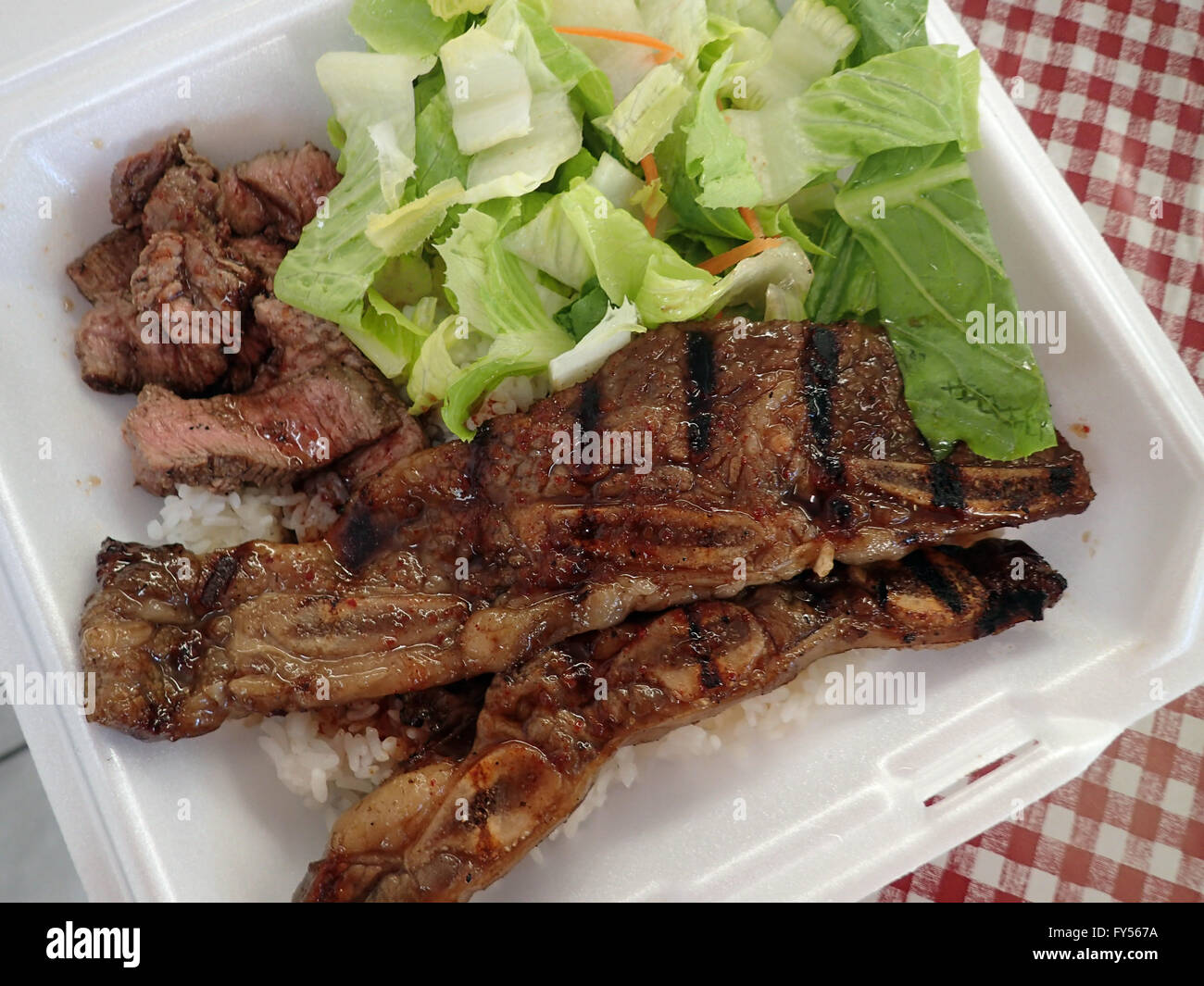 Steak, Kalbi, Side salad and white rice in a styrofoam plate. Stock Photo