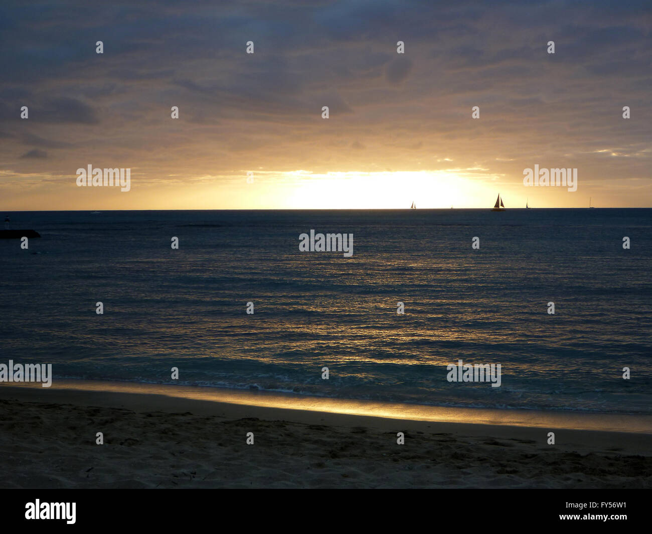 Dramatic Sunset on Queens Waikiki Beach over the ocean with boats sailing on the water and clouds hanging in the sky on Oahu, Ha Stock Photo