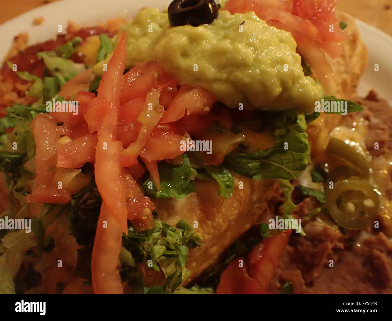 Close-up of Chimichanga topped with salsa, guacamole with spanish rice, beans, on table. Stock Photo