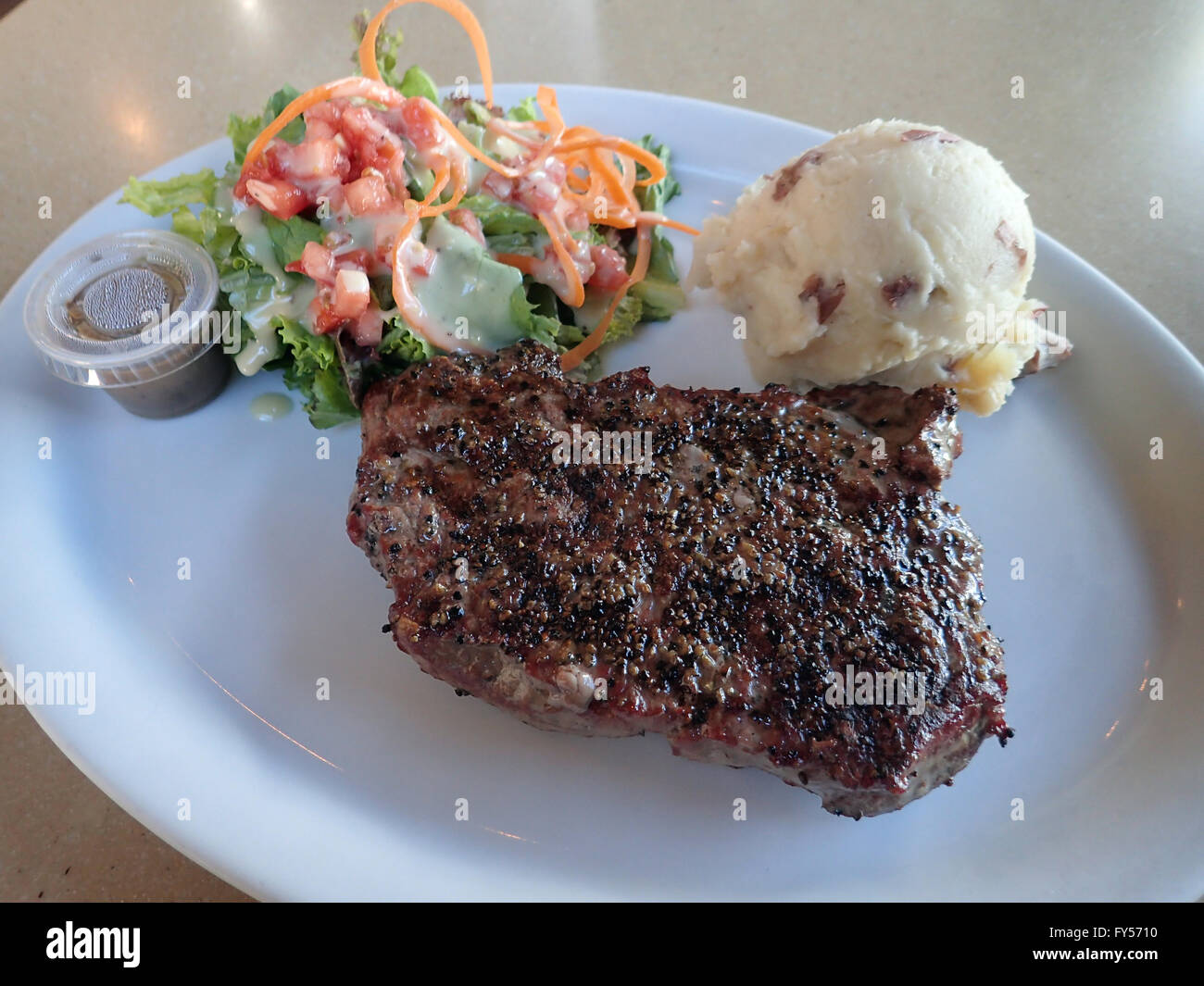 New York Steak, Mashed Potato, and Salad on white plate with dressing on a table. Stock Photo