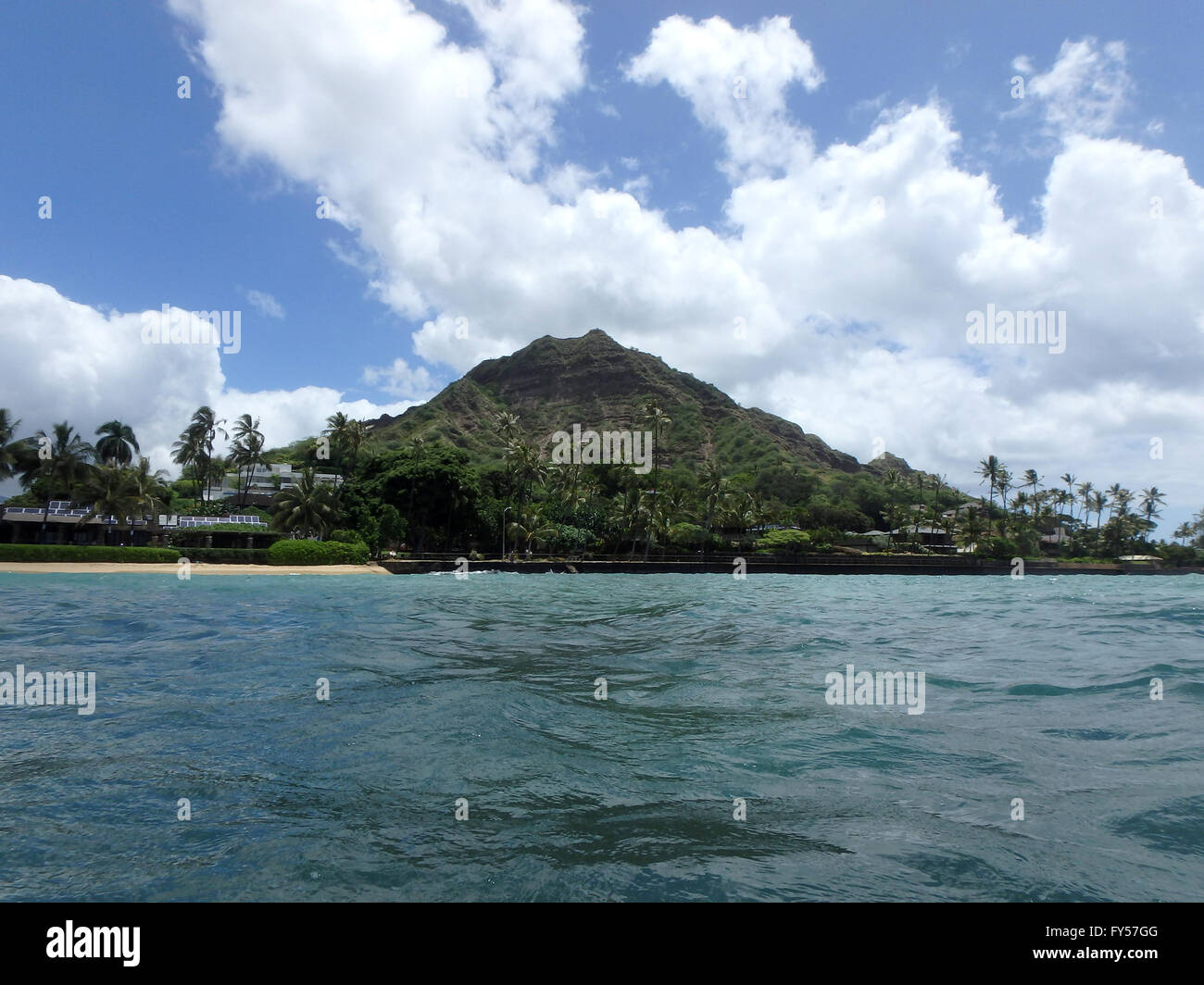 Beach and Makalei Beach Park with seawall, coconut trees, homes, and Diamond Head Crater in the distance and clouds in the sky o Stock Photo