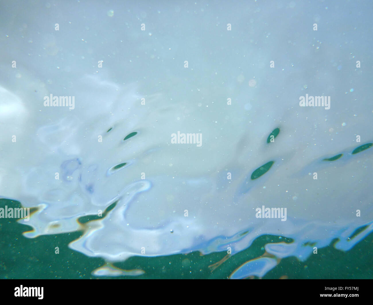 Looking through ocean water at blue sky with water ripples and air bubbles from underwater. Stock Photo