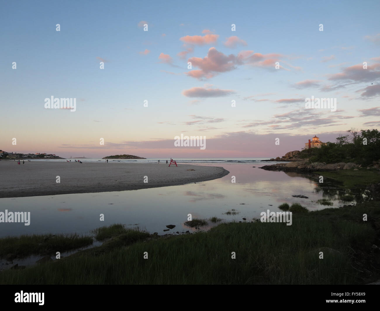 Stream leading to beach with people playing in the surf at Good Harbor Beach, Gloucester, Massachusetts during dusk. With Lifegu Stock Photo