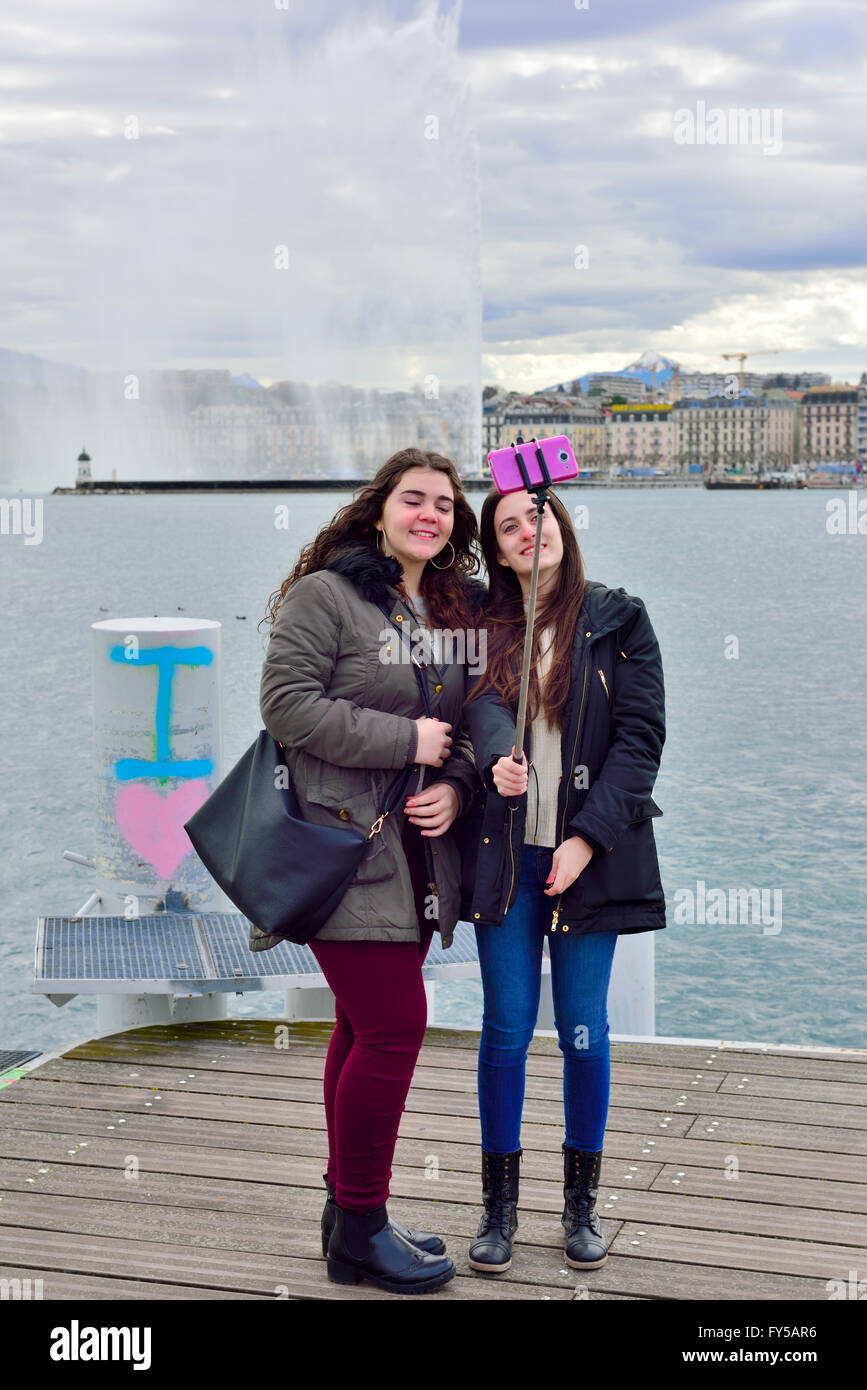 Two women taking a selfie photo with the Geneva water jet fountain across the lake in background Stock Photo