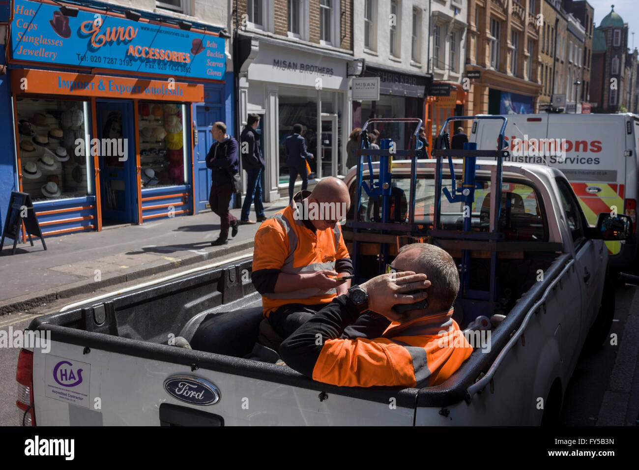 Two workmen sit in the back of their truck during a break of their