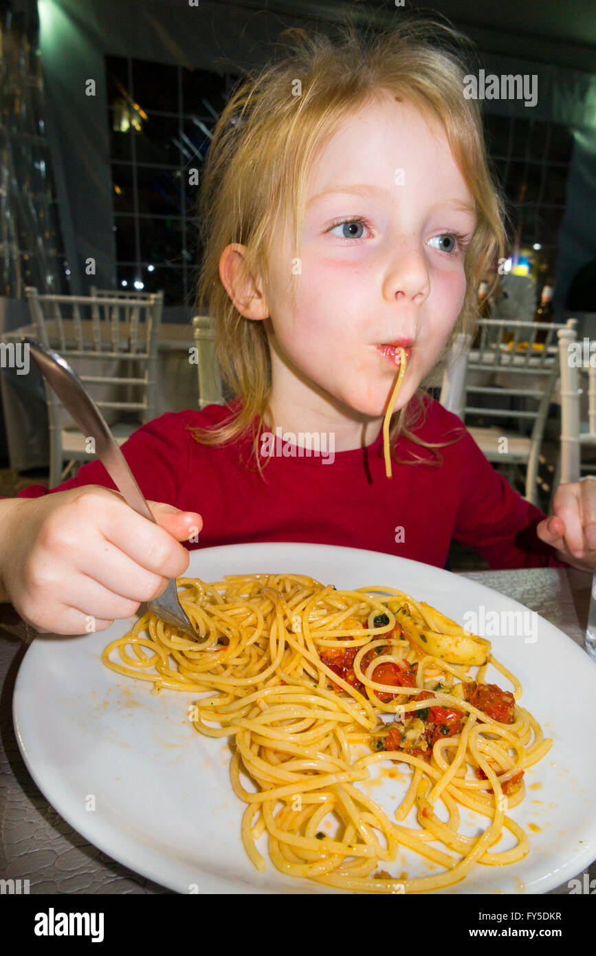 Young child girl kid / kids aged 5 - 6 year old eating authentic genuine spaghetti in Italian pasta restaurant in Naples Italy Stock Photo