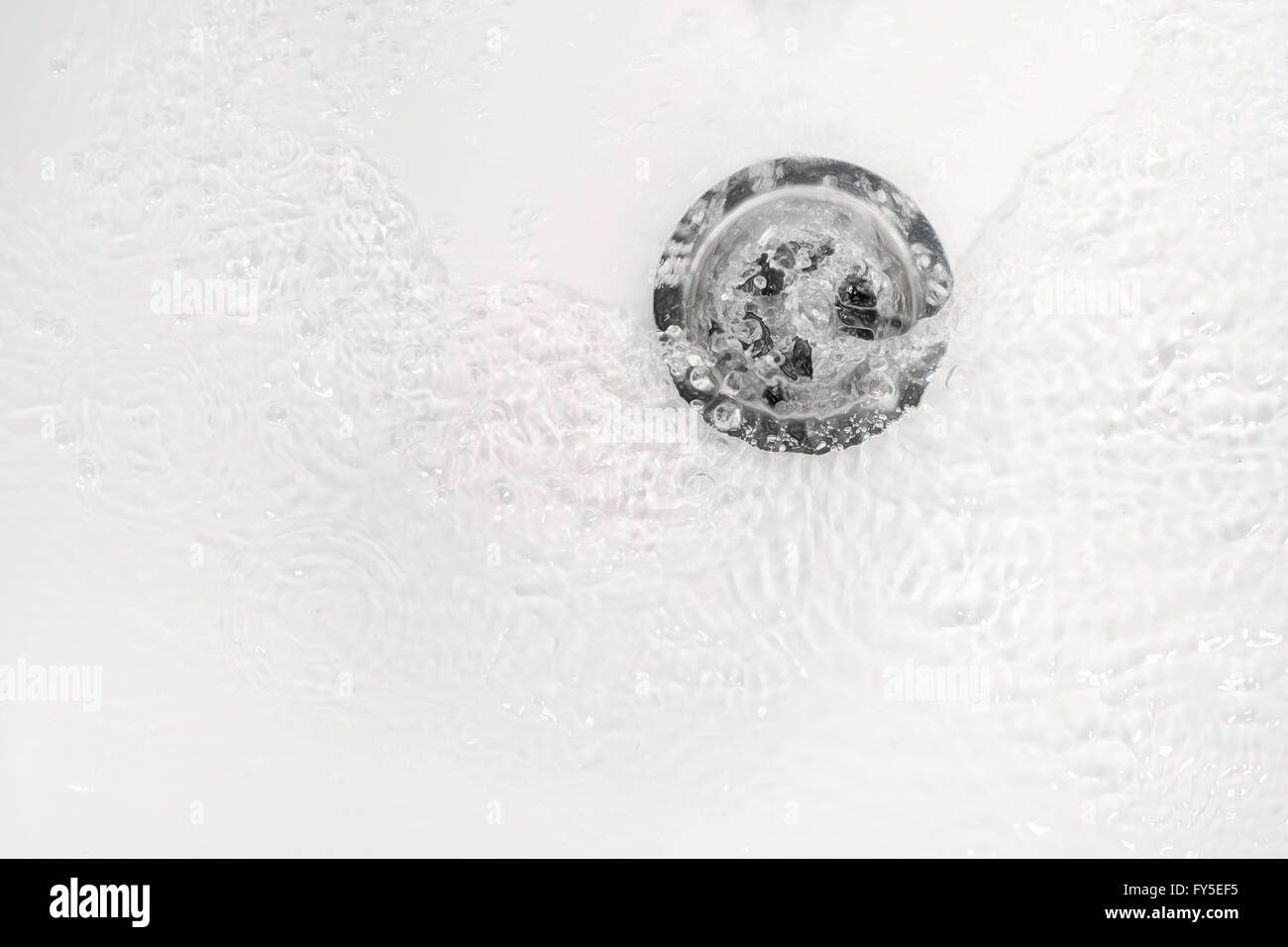 White bathroom sink drain close up with water ripple and bubbles Stock Photo