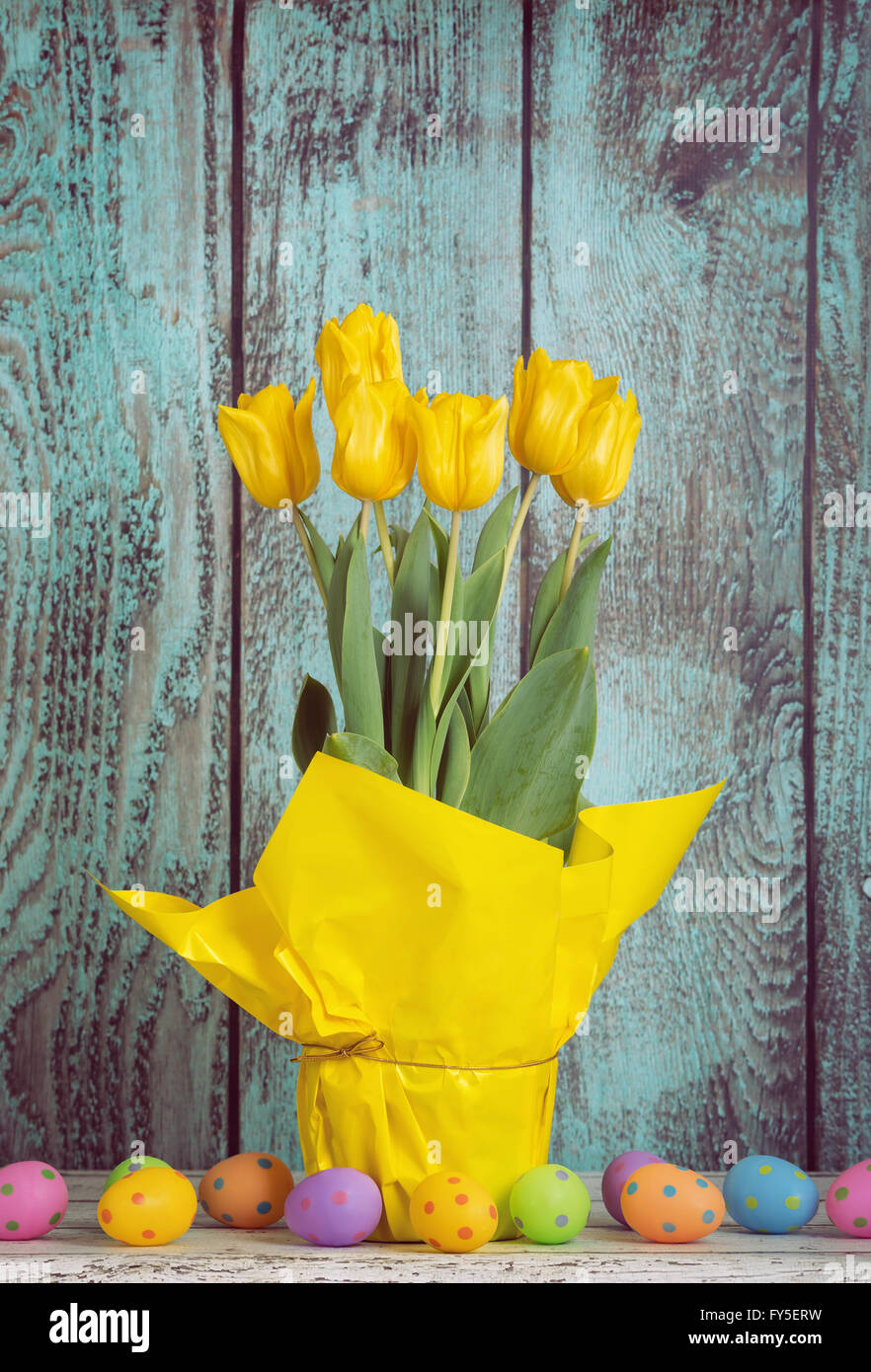 A pot of yellow Easter tulips and colorful eggs against wooden vintage ...