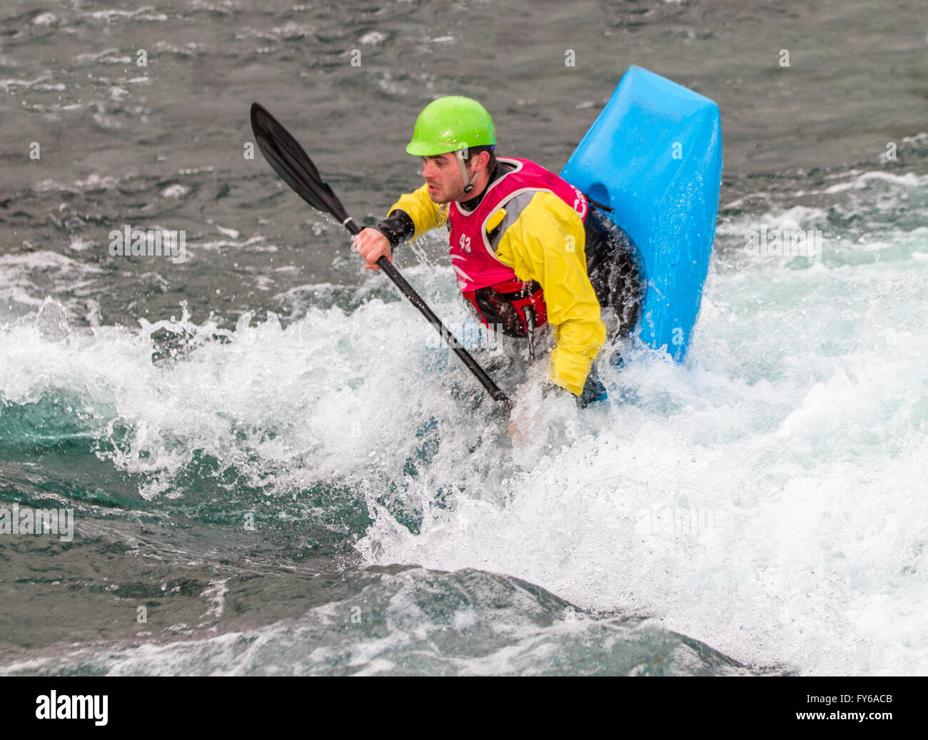 Young male man paddling a kayak in white water. The kayak is upright