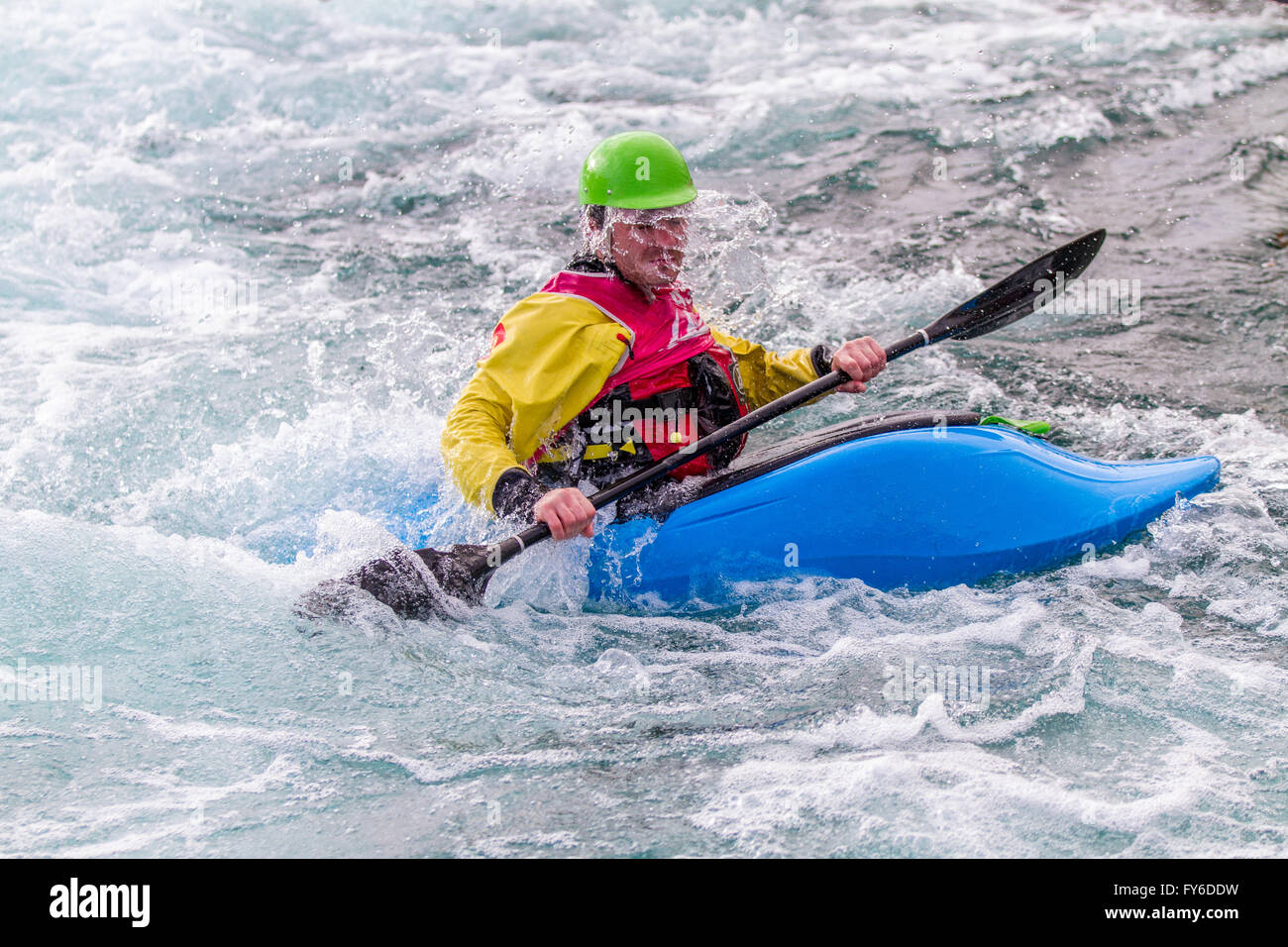 Young male man paddling a kayak in white water.  The water is falling out of the man's safety hat and running down his face. Stock Photo