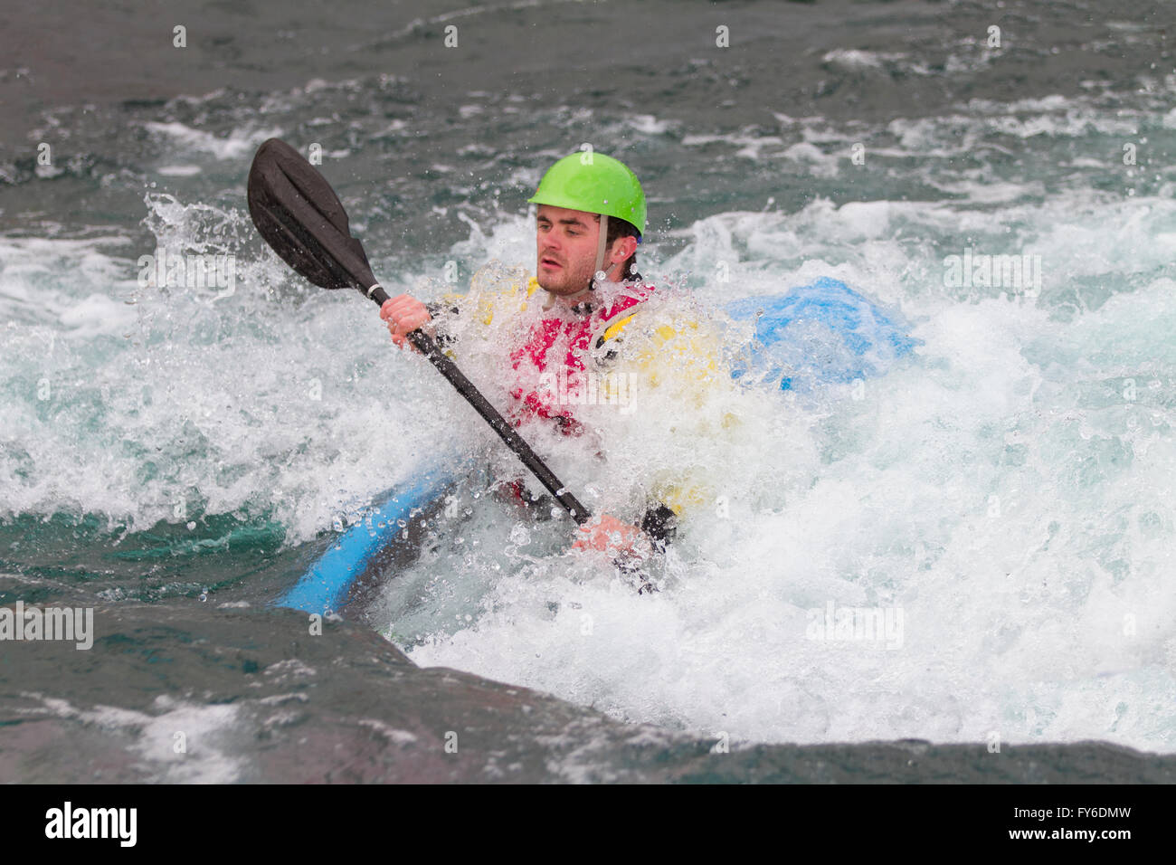 Young male man paddling a kayak in white water.  The water is swallowing up and the kayak is most submerged as he approaches the Stock Photo
