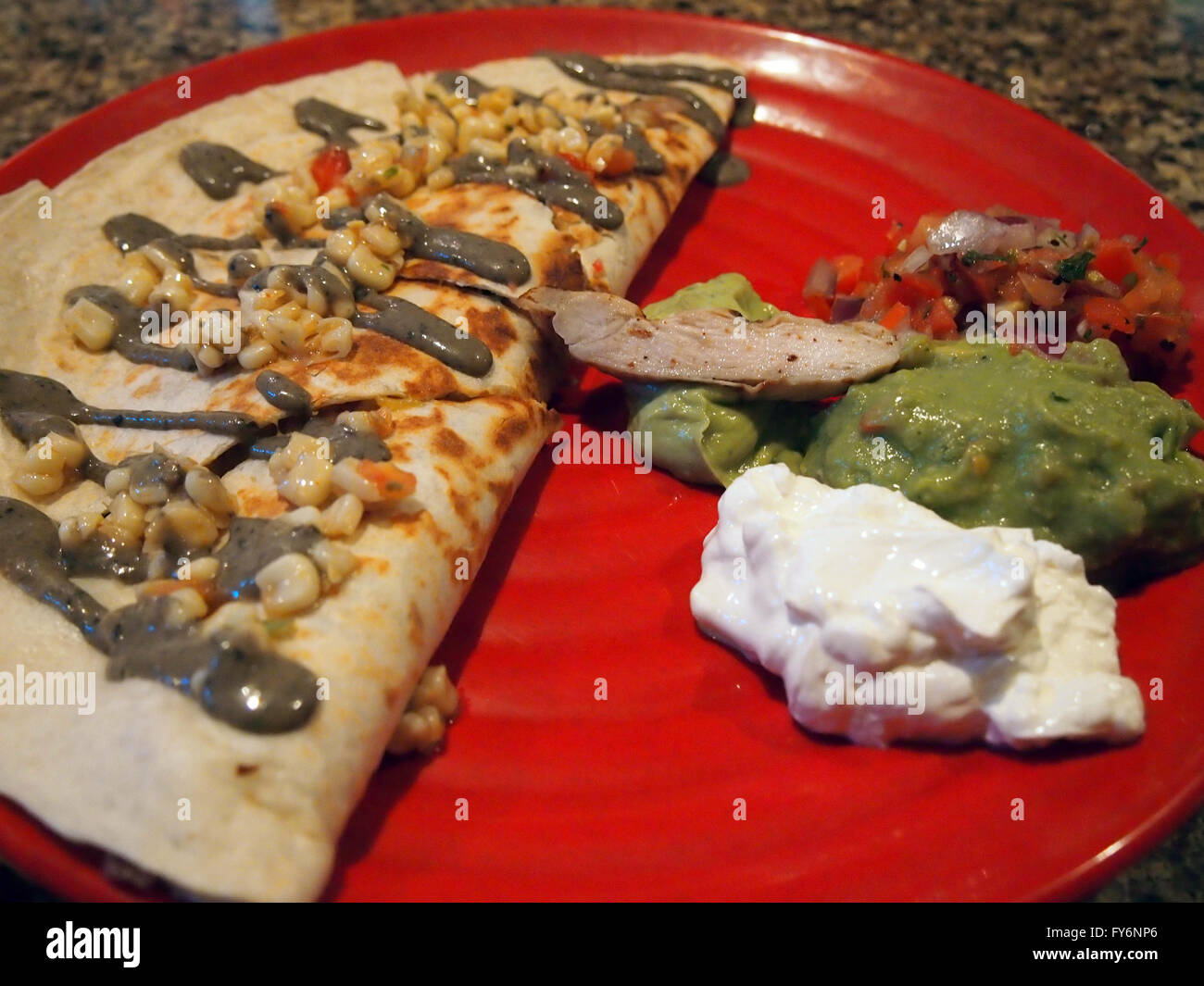 Chicken Quesadilla with corn and sauce on top and sour creme guacamole, and pico de gallo on a red plate. Stock Photo