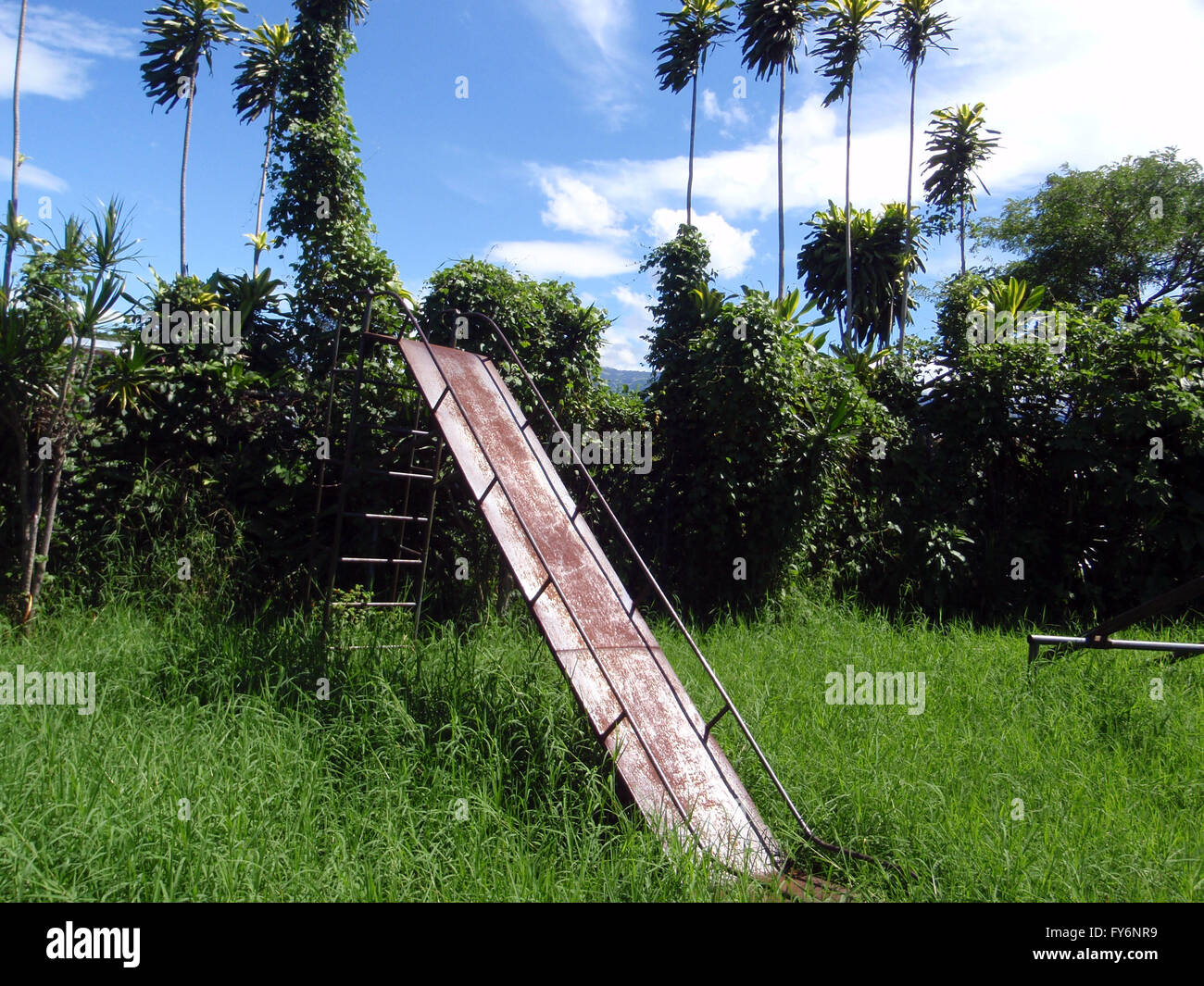 Rusted slide in overgrown grass in Heredia, Costa Rica. Stock Photo