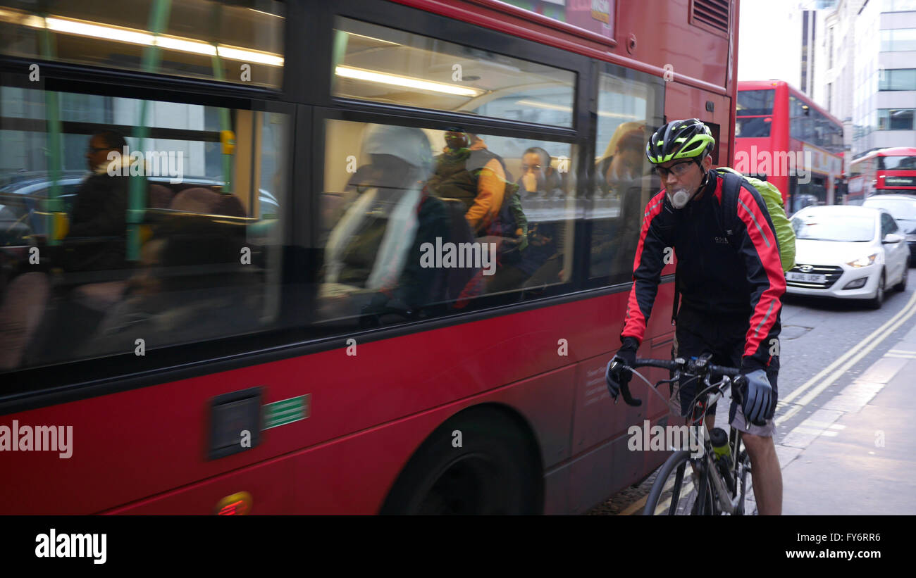 Cyclist with anti pollution smog mask, pushed off road by bus, on City of London street Stock Photo
