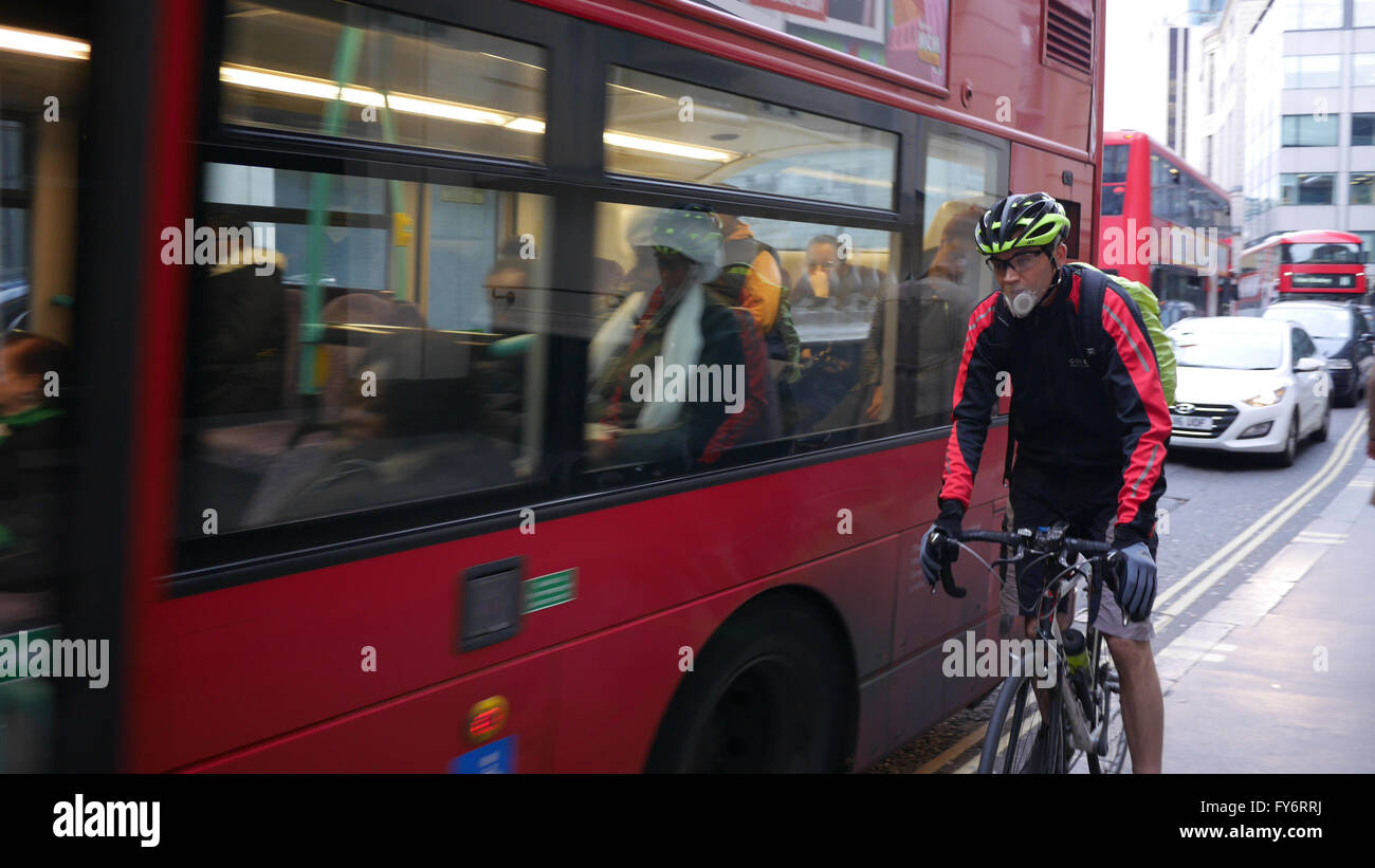 Cyclist with anti pollution smog mask, pushed off road by bus, on City of London street Stock Photo