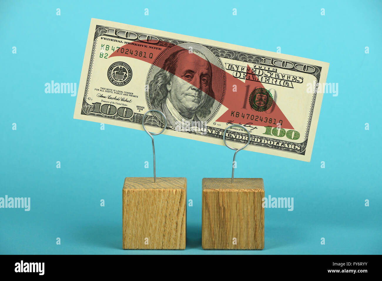 US crisis, decline of American dollar, one hundred US dollars banknote with red arrow down on wooden metal holders over blue Stock Photo