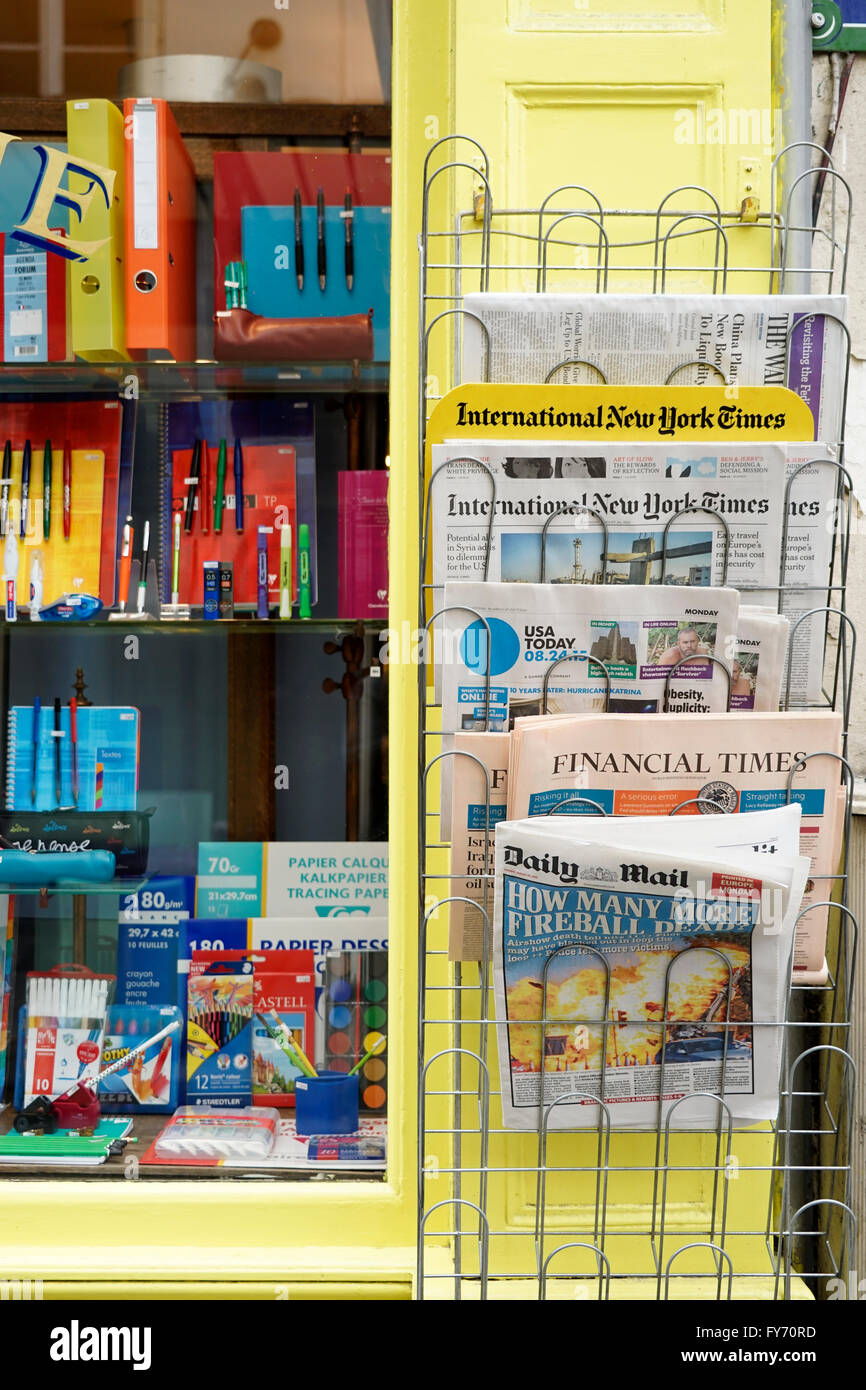 Window of stationery store with newspapers in different languages display beside in Saint