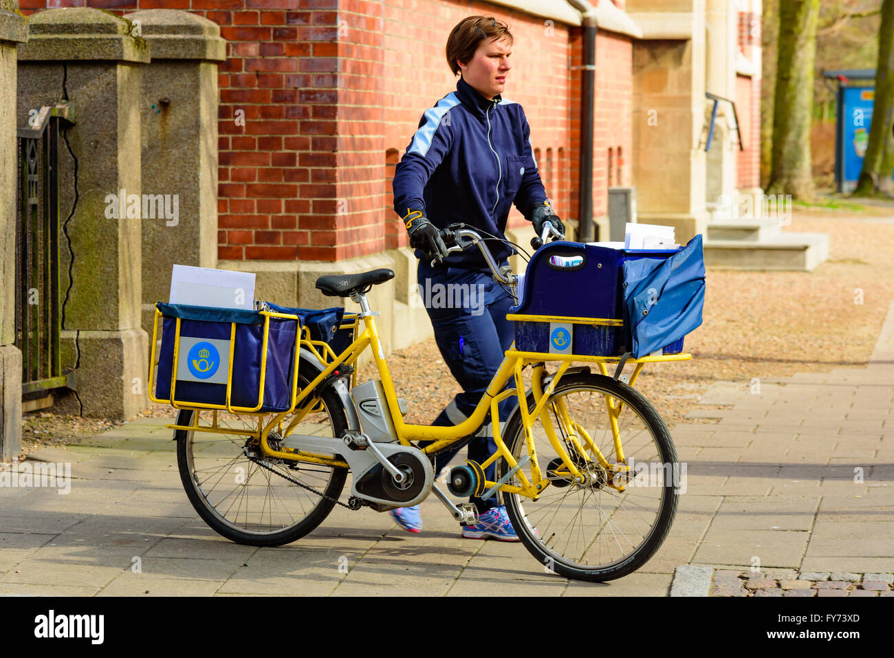Trelleborg, Sweden . April 12, 2016: Female mailman pushing a bike full of mail and letters across the pavement. Stock Photo