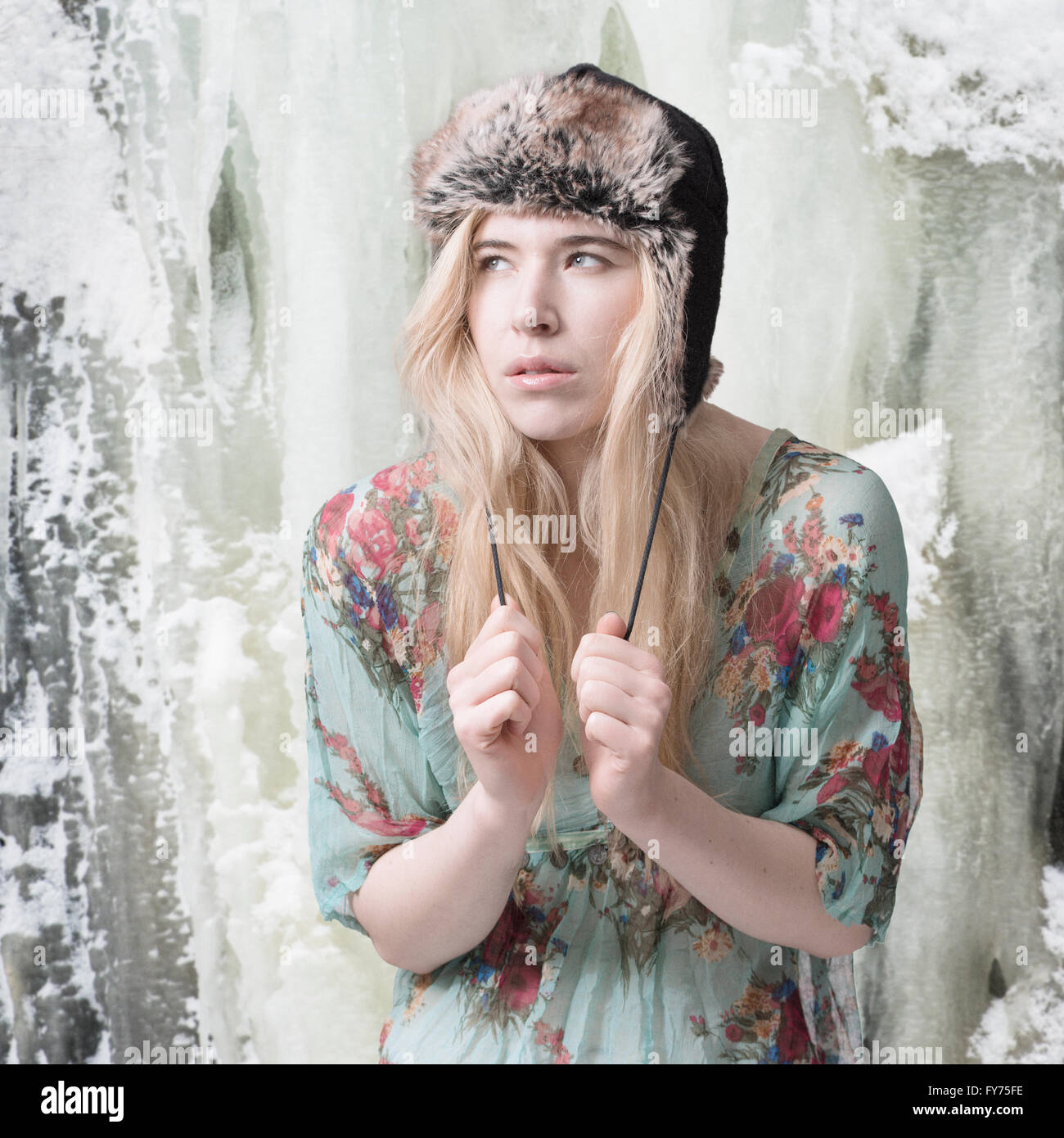 Blond woman summer dress and winter hat, in front of an ice-covered mountain Stock Photo