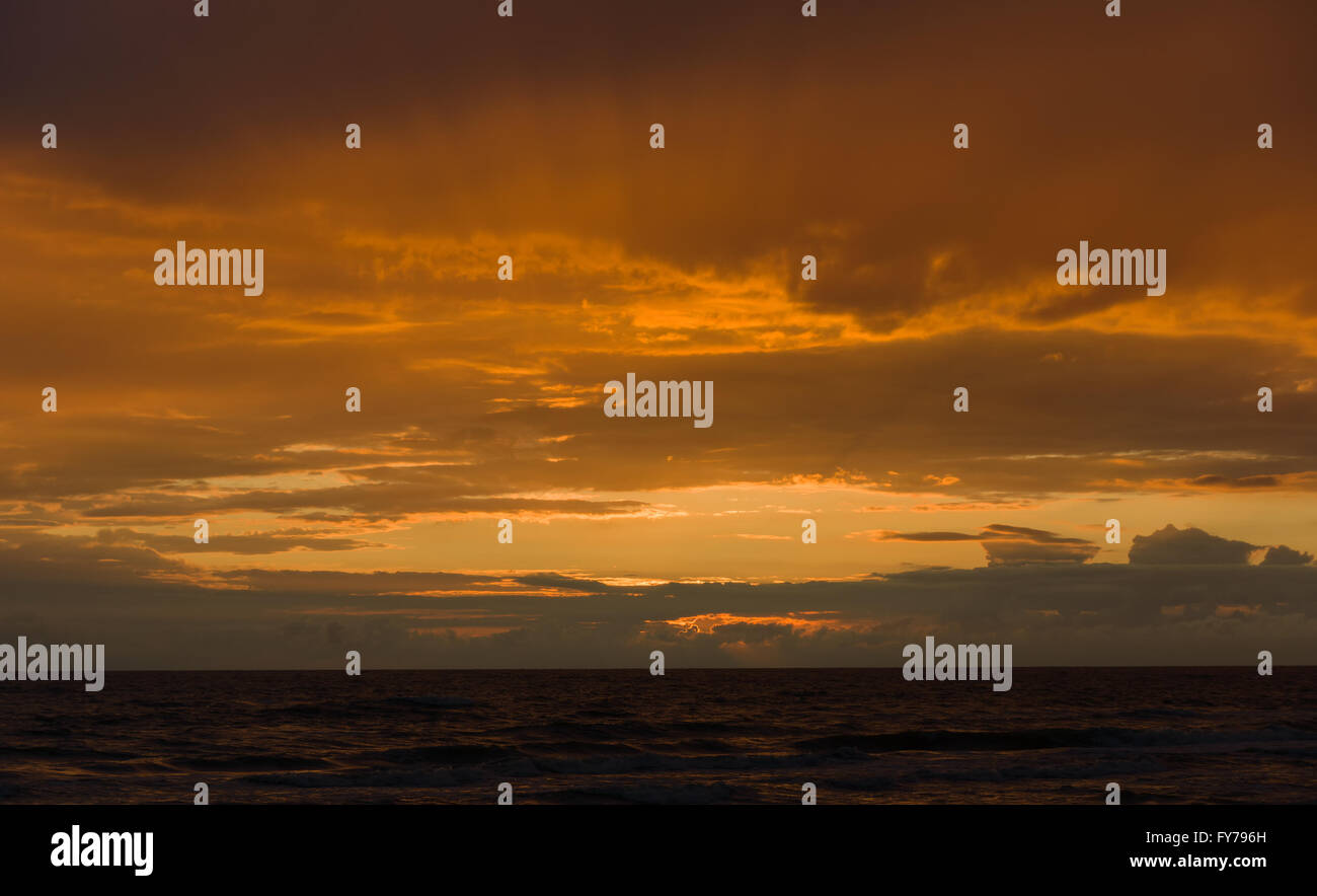 the sun sits down over the sea drawing silhouettes ashore Stock Photo