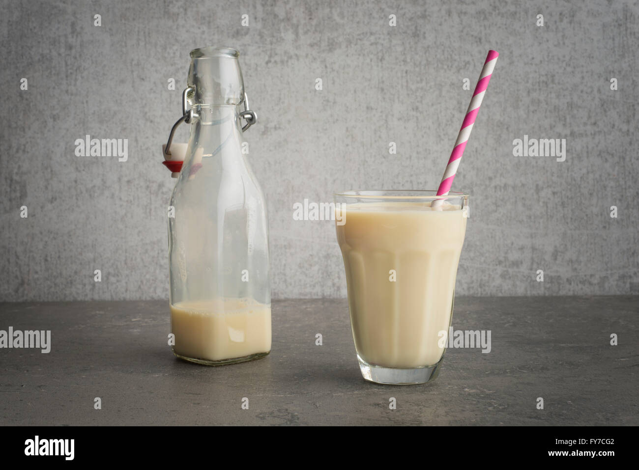 Soy milk in a glass with striped drinking straw and glass bottle on stone table. Stock Photo