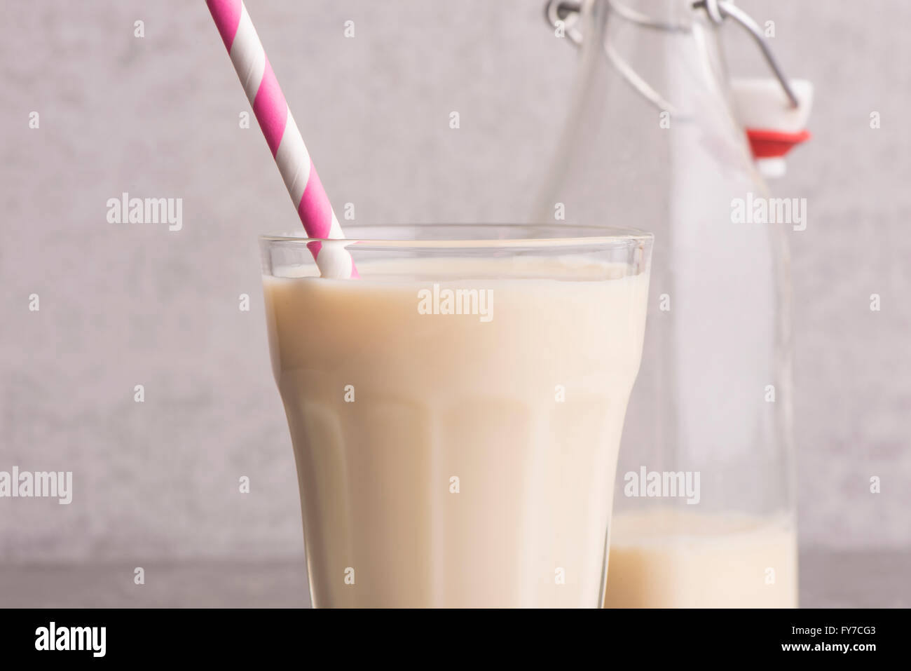 Soy milk in a glass with striped drinking straw and glass bottle on stone table. Stock Photo