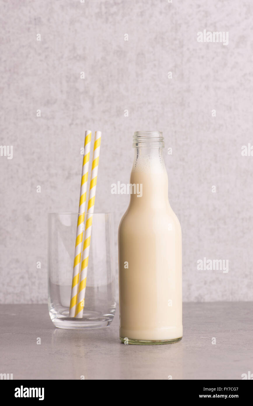 Soy milk in a glass bottle with empty drinking glass and striped straws on stone table. Stock Photo