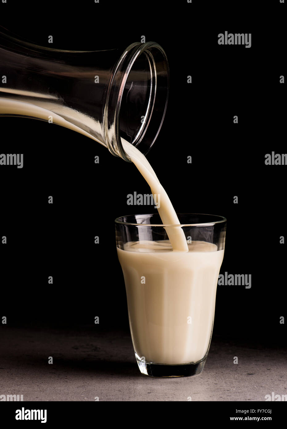 Oat milk being poured from bottle in a drinking glass. Black background. Stock Photo