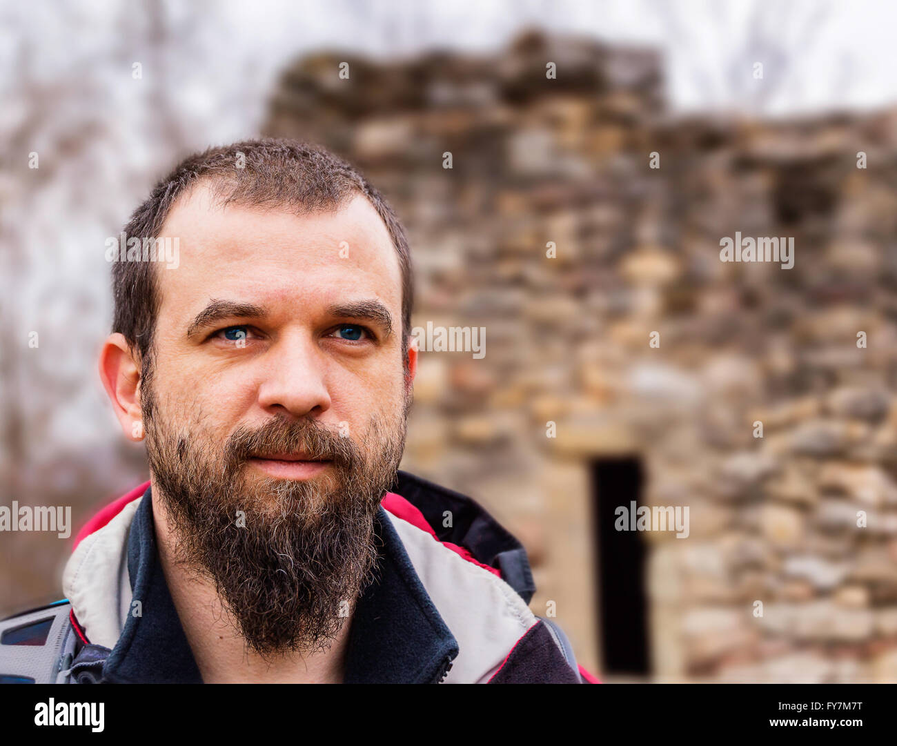 Blue eyed bearded man closeup in front of a stone ruined castle. Stock Photo
