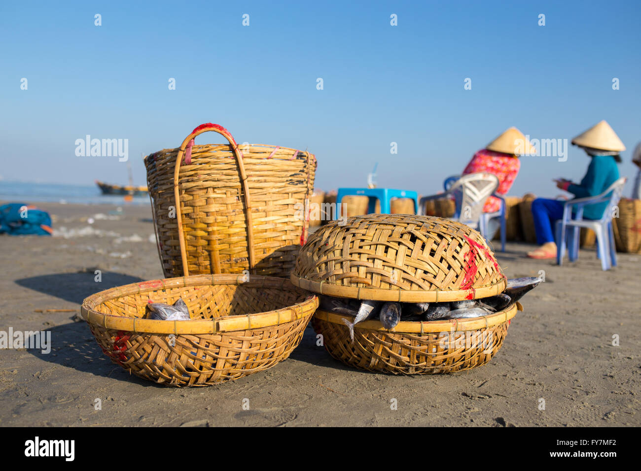 Fishing basket with two woman, wearing conical hat in background under blue sky at Long Hai beach, Ba Ria, Vung Tau, VietNam Stock Photo